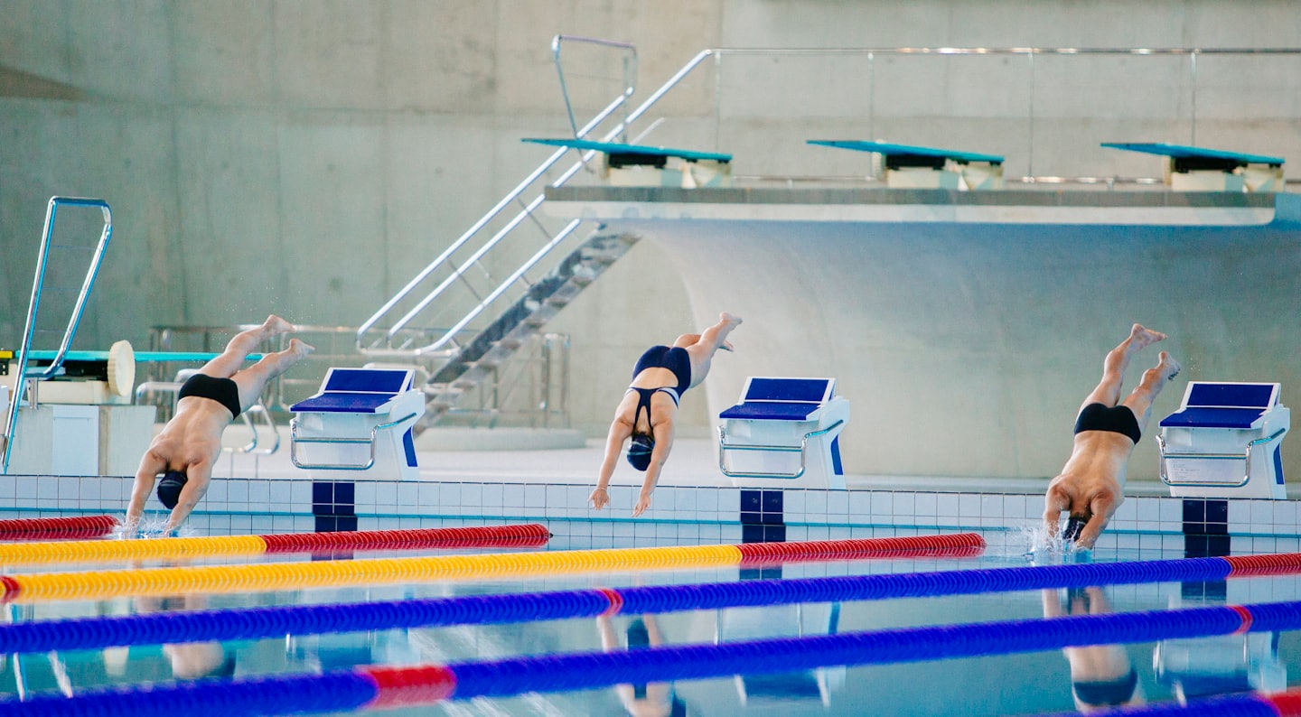 Des nageurs plongent dans une piscine intérieure bien éclairée.
