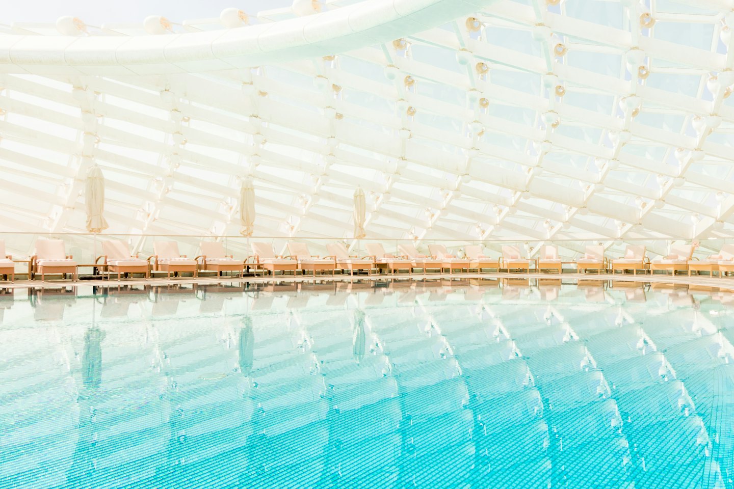 Chaises longues vides au bord d'une piscine intérieure lumineuse.