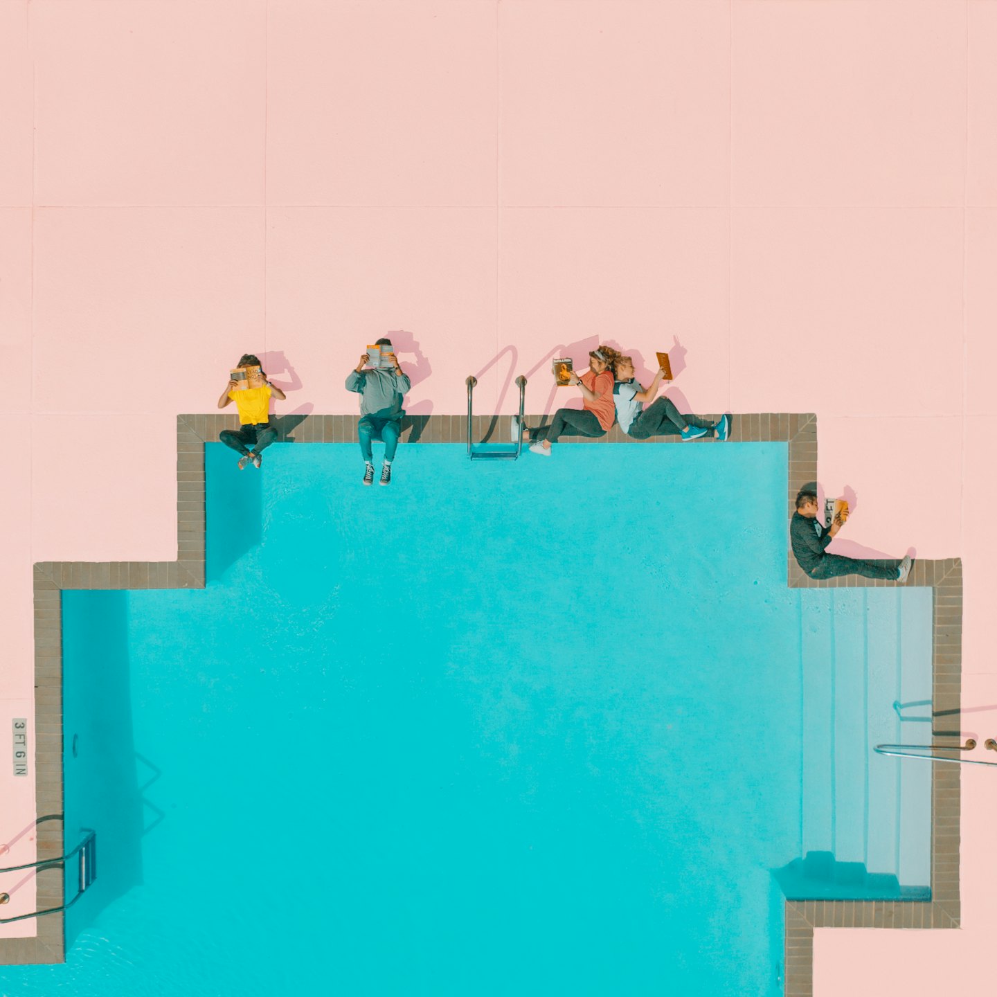 Cinq personnes lisent des livres au bord d'une piscine turquoise.