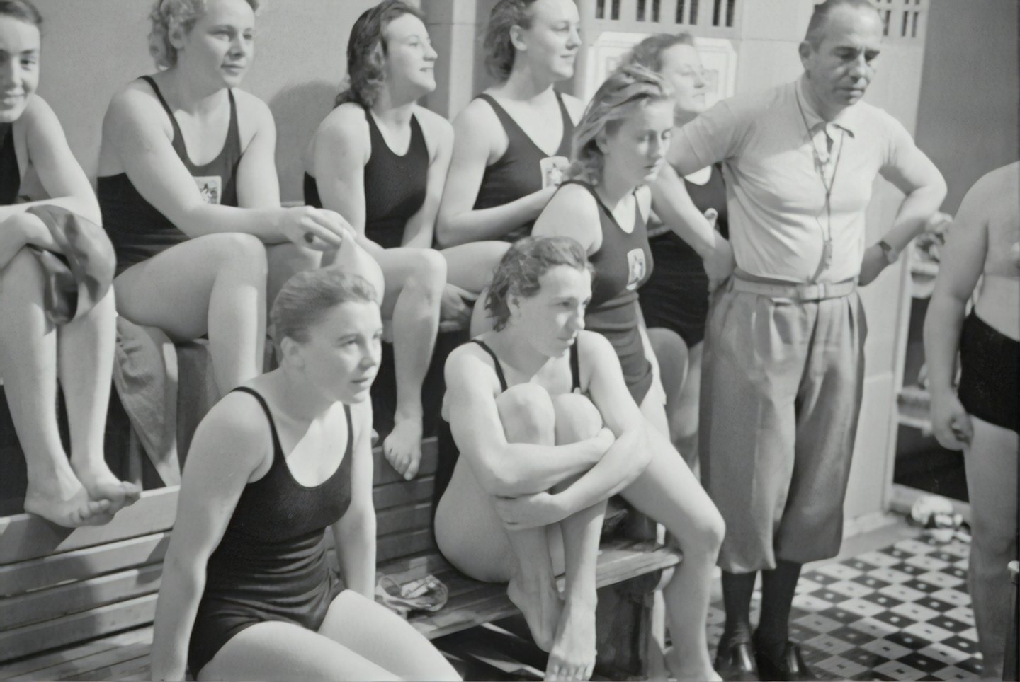 Des nageurs écoutent leur entraîneur au bord de la piscine intérieure.